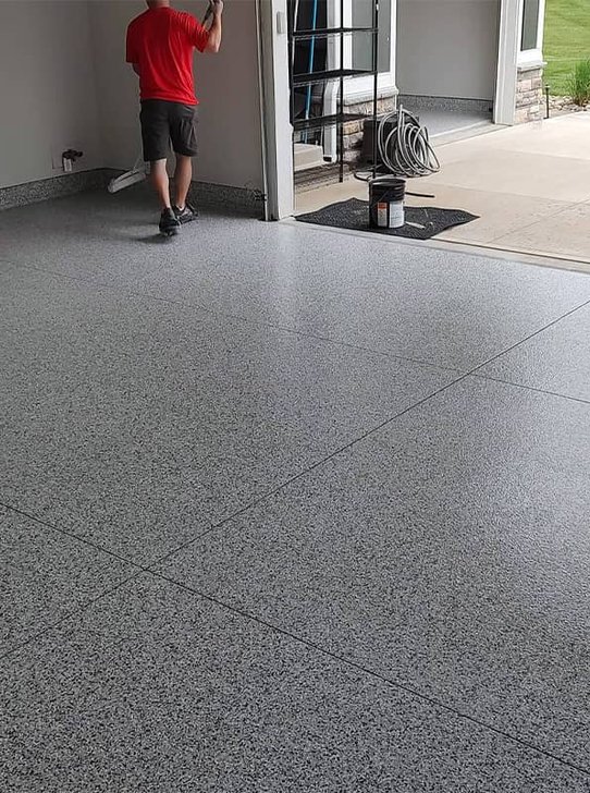 Installer applying a gray flake epoxy coating in an open garage